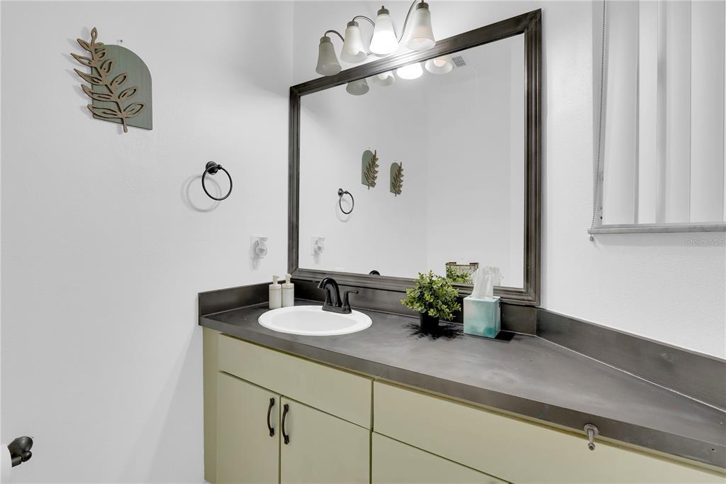 A bathroom features a sage green vanity with a dark countertop and a large mirror — 4703 VERO BEACH PLACE, KISSIMMEE, FL