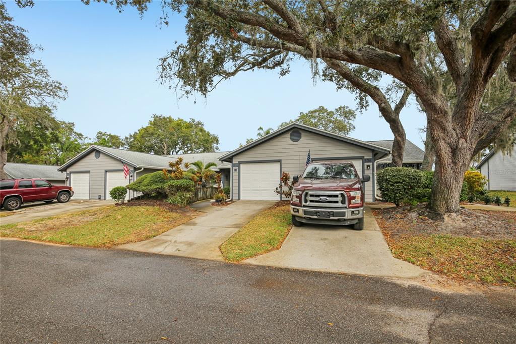 A single-story duplex with two garages, concrete driveways, and large oak trees in the yard — 39650 US HIGHWAY 19 HIGHWAY N UNIT 135, TARPON SPRINGS, FL