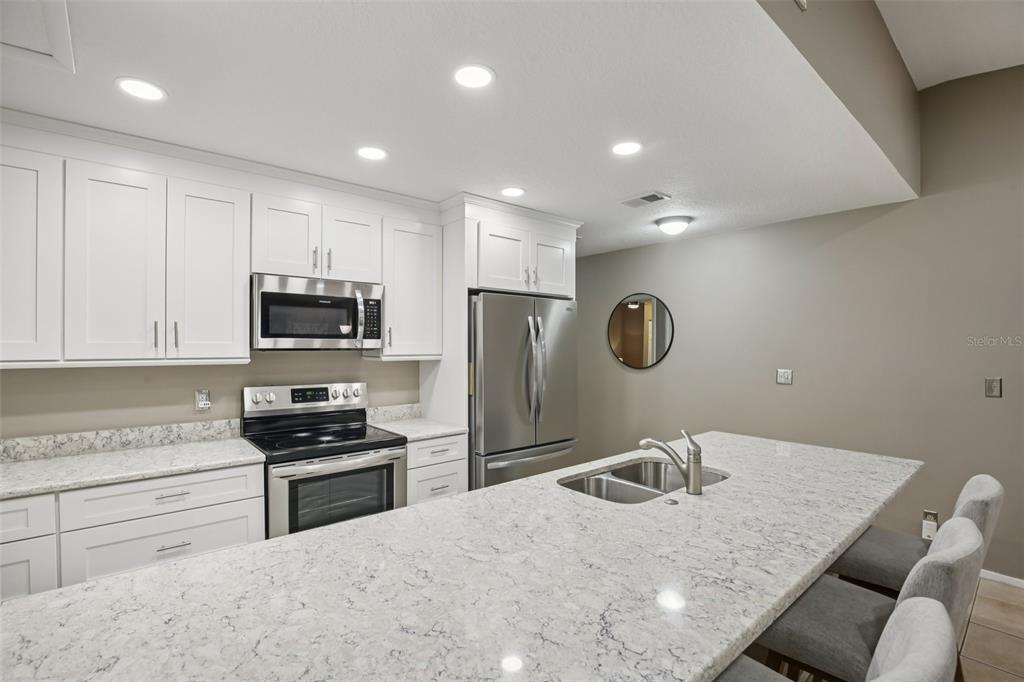 A modern kitchen features white cabinets, granite countertops, stainless steel appliances, and a central island — 39650 US HIGHWAY 19 HIGHWAY N UNIT 135, TARPON SPRINGS, FL
