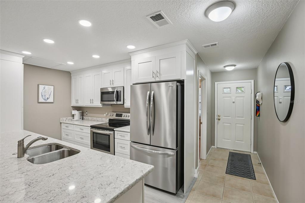 A kitchen features white cabinets, stainless steel appliances, and a granite-topped island with a sink — 39650 US HIGHWAY 19 HIGHWAY N UNIT 135, TARPON SPRINGS, FL