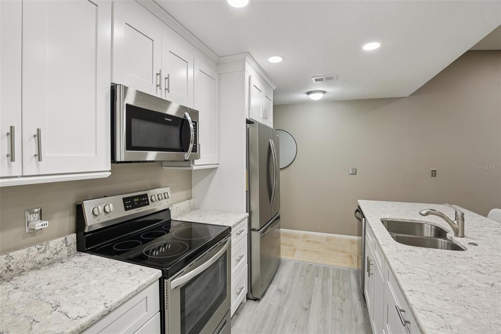 A kitchen features white cabinets, stainless steel appliances, and speckled granite countertops — 39650 US HIGHWAY 19 HIGHWAY N UNIT 135, TARPON SPRINGS, FL