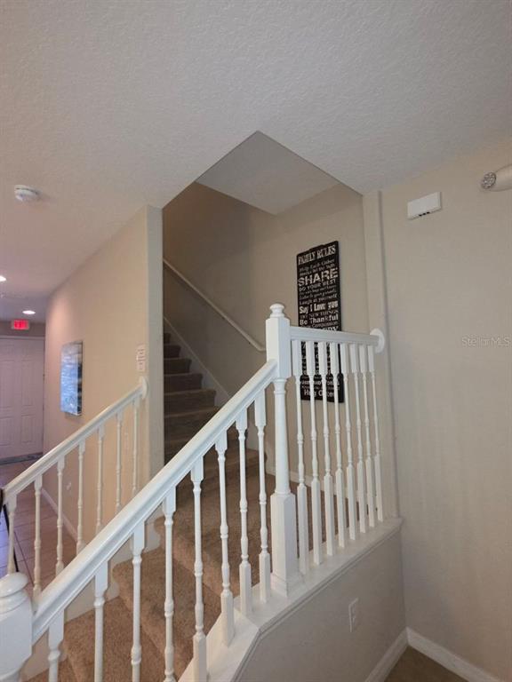 A carpeted staircase with white wooden railings leads to an upper level in a home — 4746 TERRASONESTA DRIVE, DAVENPORT, FL