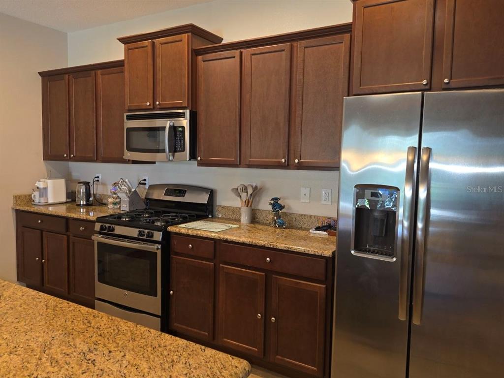A kitchen features dark wood cabinets, granite countertops, and stainless steel appliances — 4746 TERRASONESTA DRIVE, DAVENPORT, FL