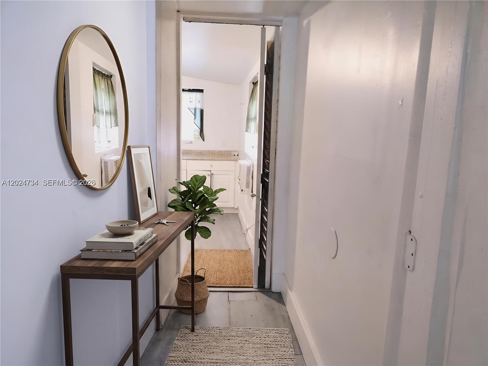 A hallway with a console table and mirror leads into a kitchen with white cabinets — 5647 NW 5th Ct # B, Miami FL 33127, MIAMI, FL