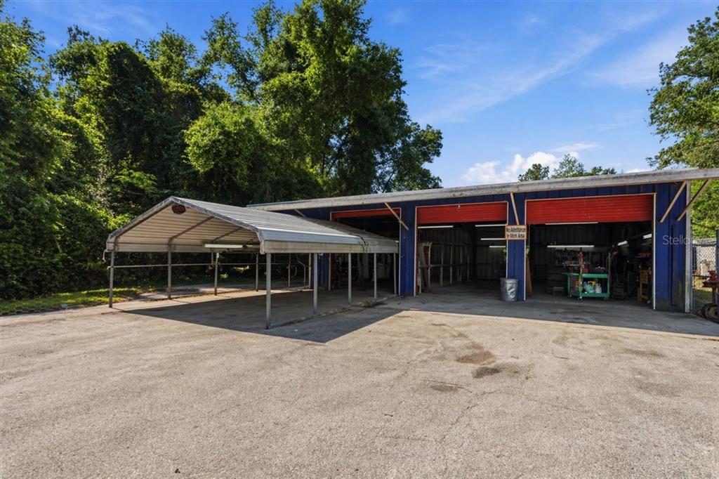 A blue metal workshop building with two open garage bays and an attached metal carport — 16260 NW US HIGHWAY 441, ALACHUA, FL