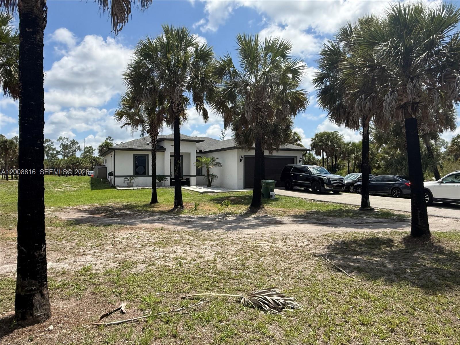 A white single-story house with a dark garage and palm trees sits on a lot — 2772 38th Ave SE, Naples FL 34117, NAPLES, FL