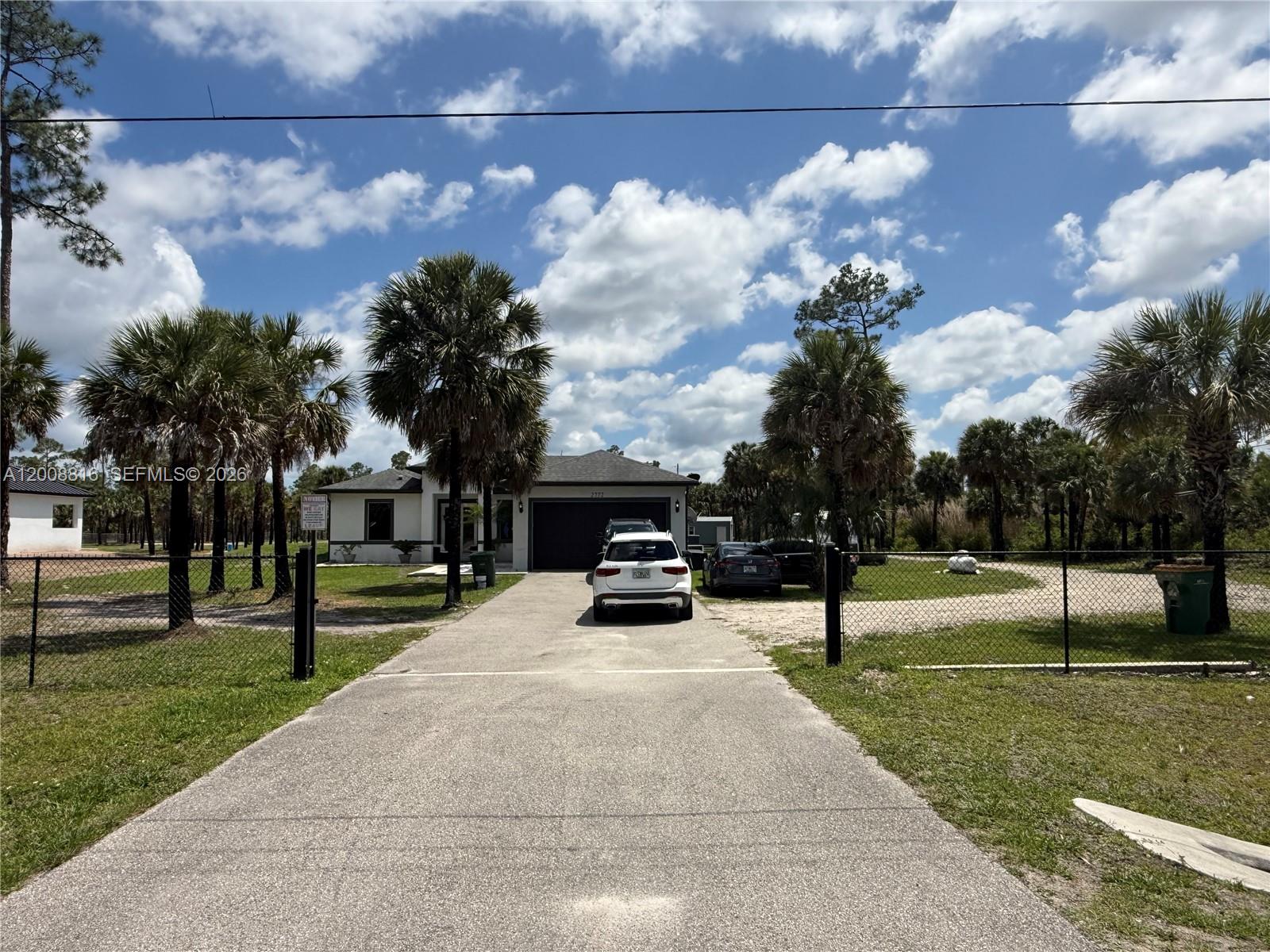 A white house with a garage and driveway sits behind a chain-link fence — 2772 38th Ave SE, Naples FL 34117, NAPLES, FL