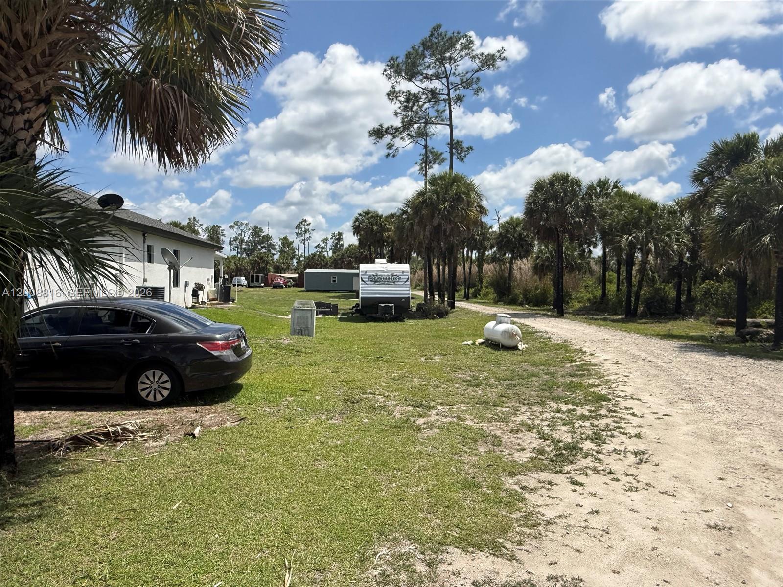 A gravel driveway leads past a parked car, a travel trailer, and palm trees — 2772 38th Ave SE, Naples FL 34117, NAPLES, FL