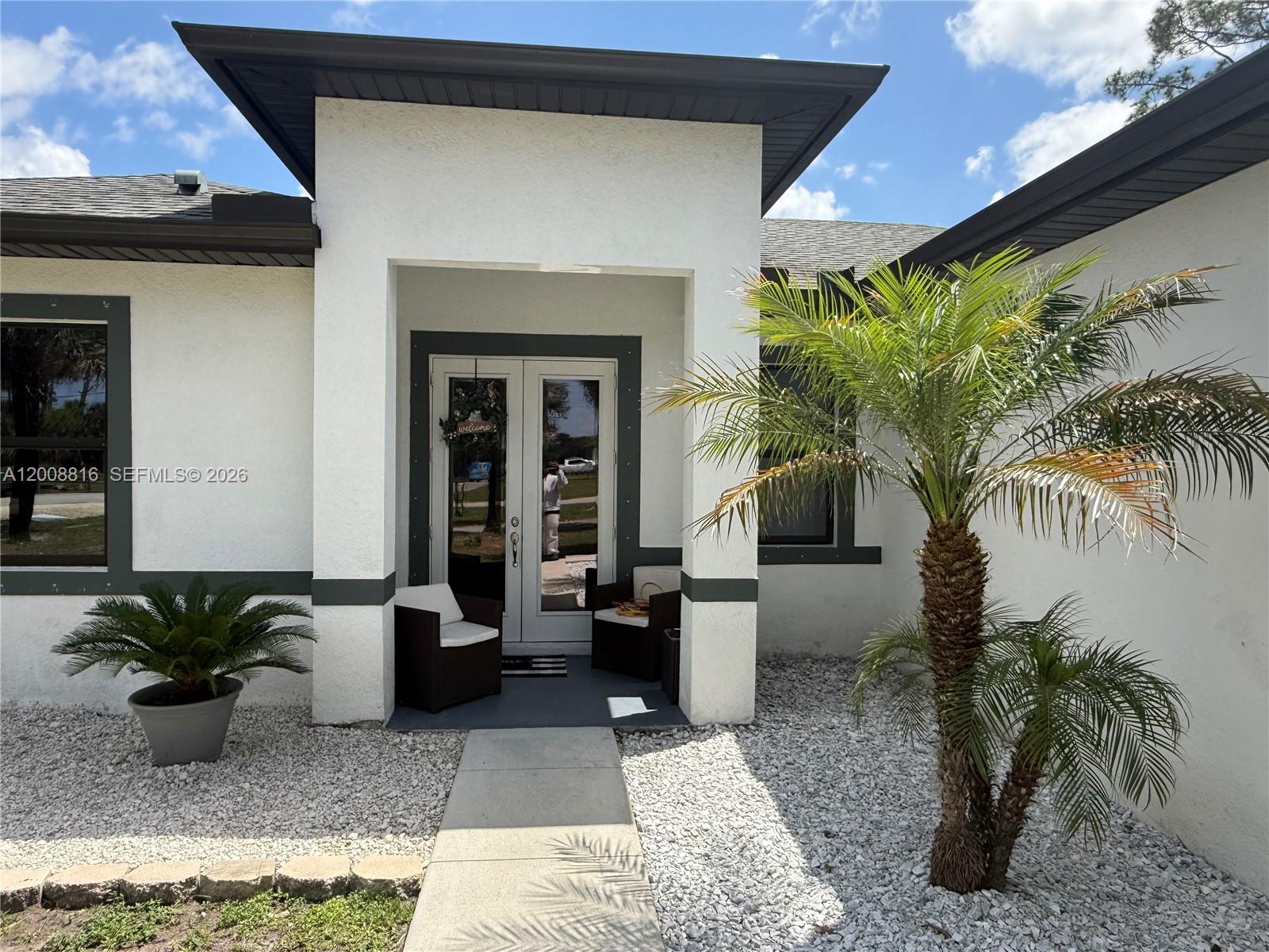 The exterior of a white house features a covered entryway with a palm tree — 2772 38th Ave SE, Naples FL 34117, NAPLES, FL