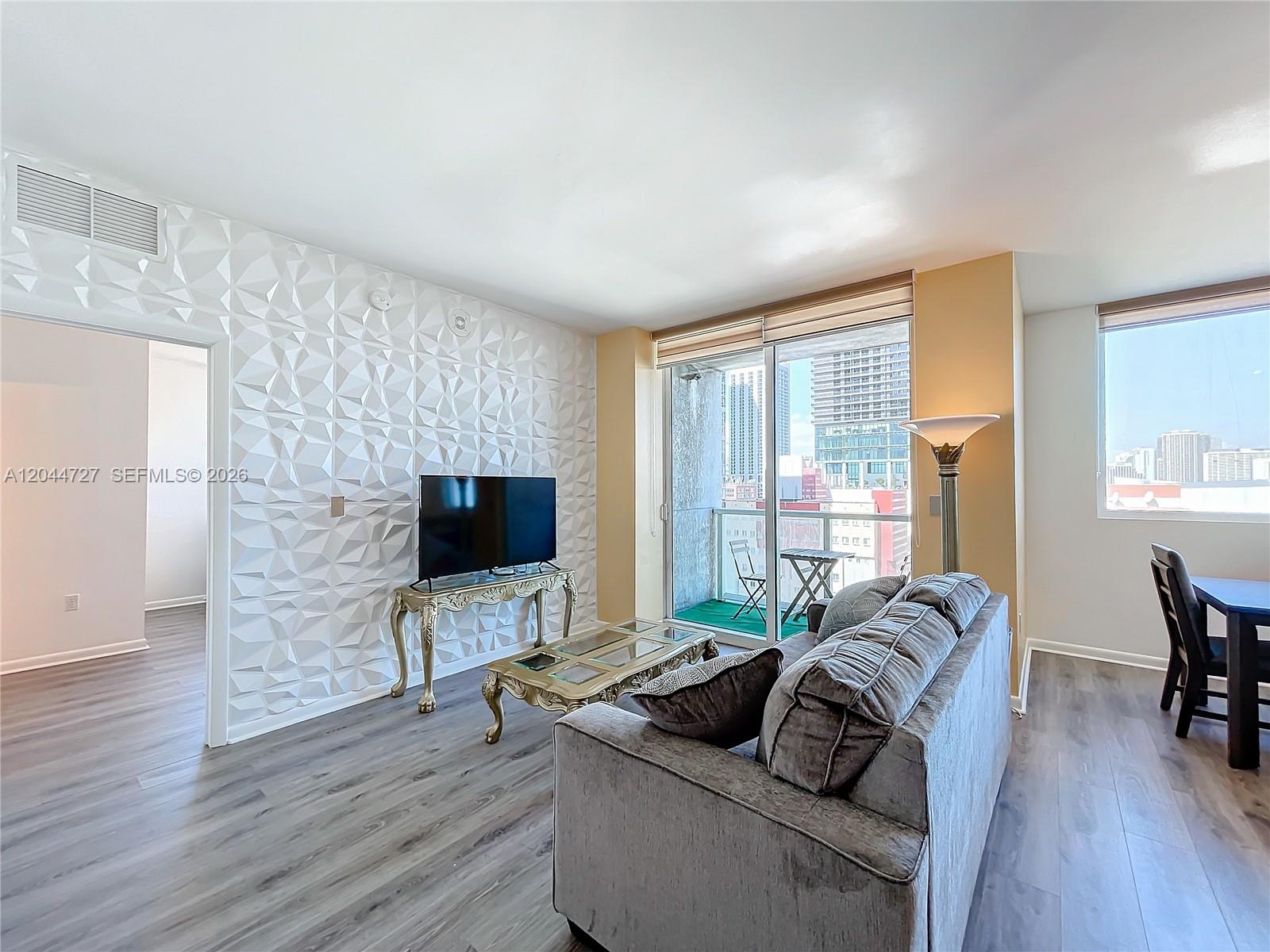 A living room features a textured accent wall, gray flooring, and a balcony with city views — 244 Biscayne Blvd # 1108, Miami FL 33132, MIAMI, FL