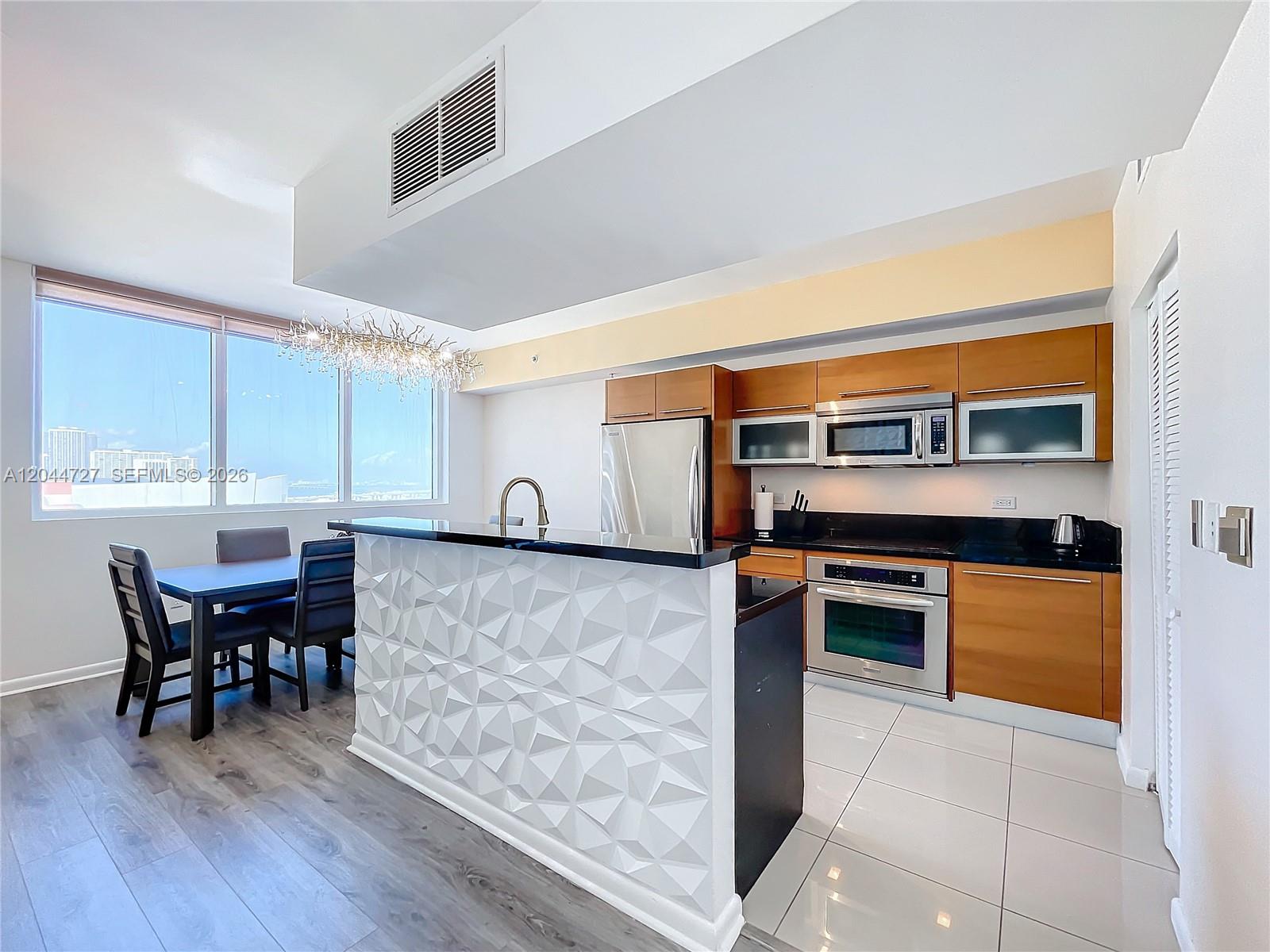 A kitchen features wood cabinets, stainless steel appliances, and a white geometric-patterned island — 244 Biscayne Blvd # 1108, Miami FL 33132, MIAMI, FL