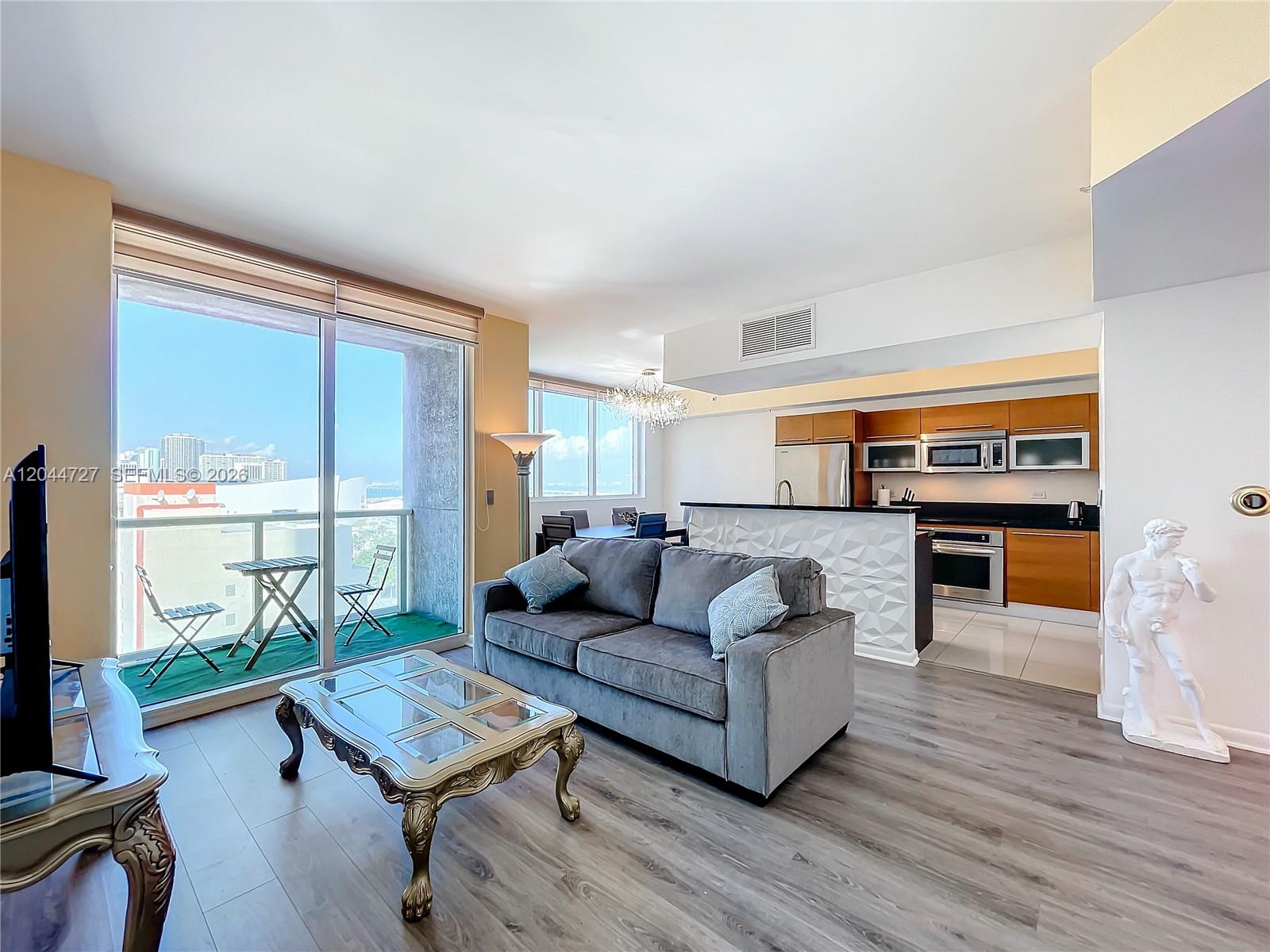 A living room with a gray sofa, glass coffee table, and an open kitchen area — 244 Biscayne Blvd # 1108, Miami FL 33132, MIAMI, FL