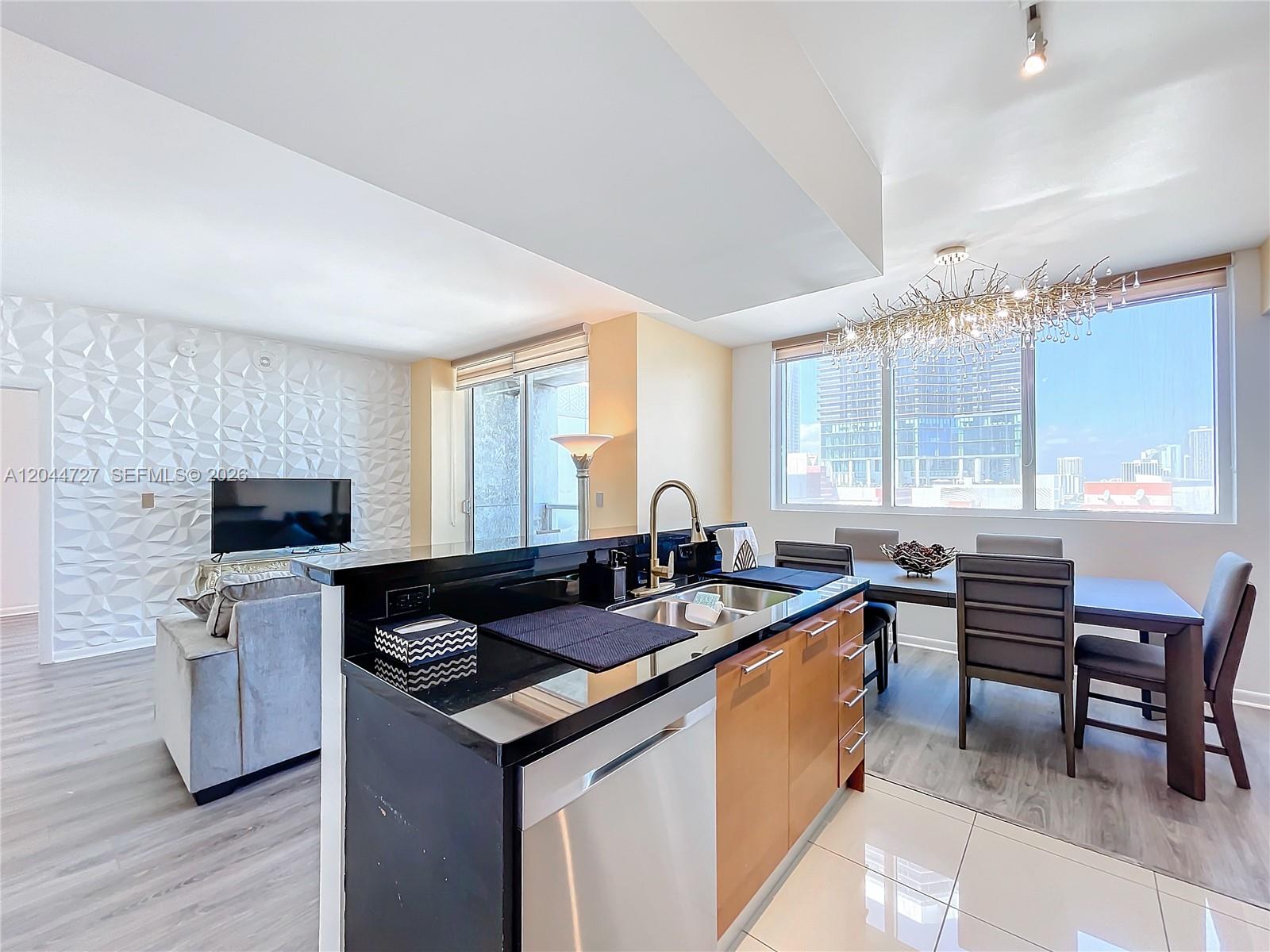 A modern kitchen with black countertops and wood cabinets overlooks a dining area and living room — 244 Biscayne Blvd # 1108, Miami FL 33132, MIAMI, FL