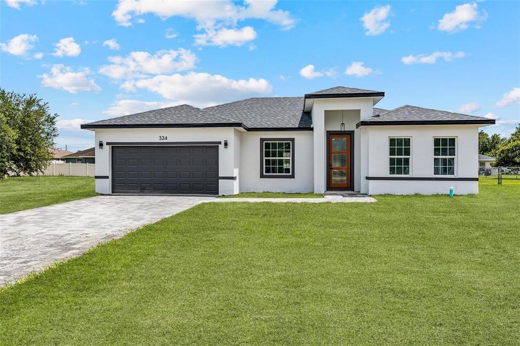 A single-story white house with a dark garage door, gray roof, and a paved driveway — 324 MARION OAKS TRAIL, OCALA, FL