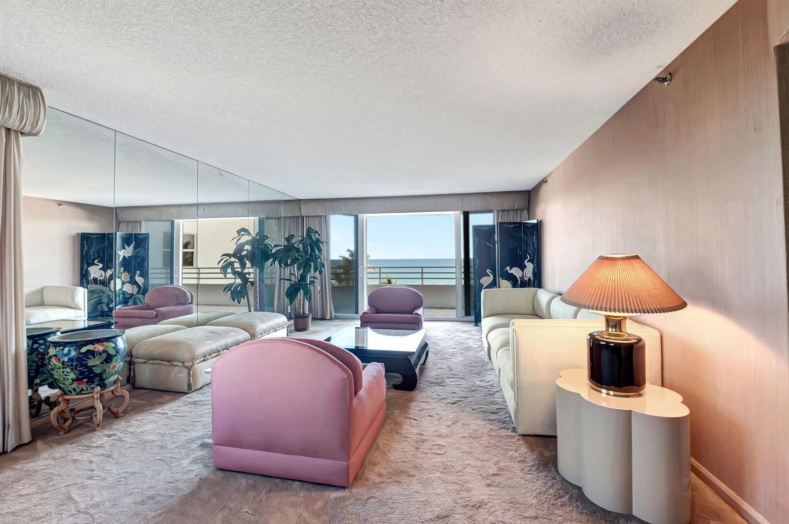 A living room with pink armchairs, a white sectional, mirrored walls, and an ocean view — 3407 S Ocean Boulevard # 4d, Highland Beach FL 33487, HIGHLAND BEACH, FL