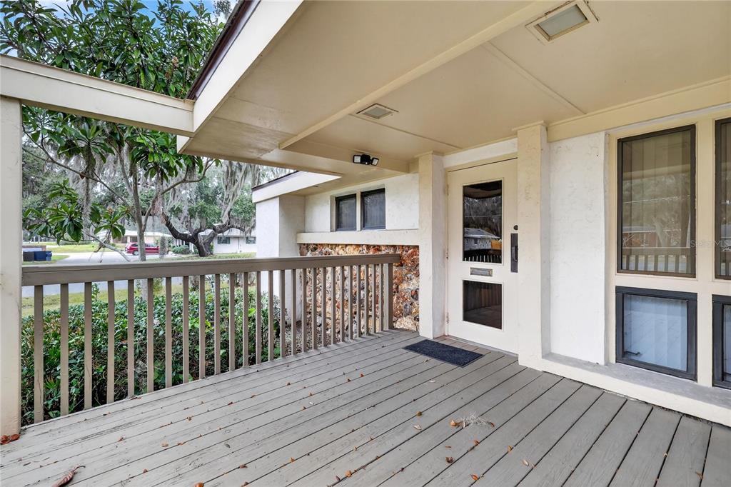 A covered wooden porch features a railing, a stone accent wall, and a glass-paneled door — 708 LEE STREET, LEESBURG, FL