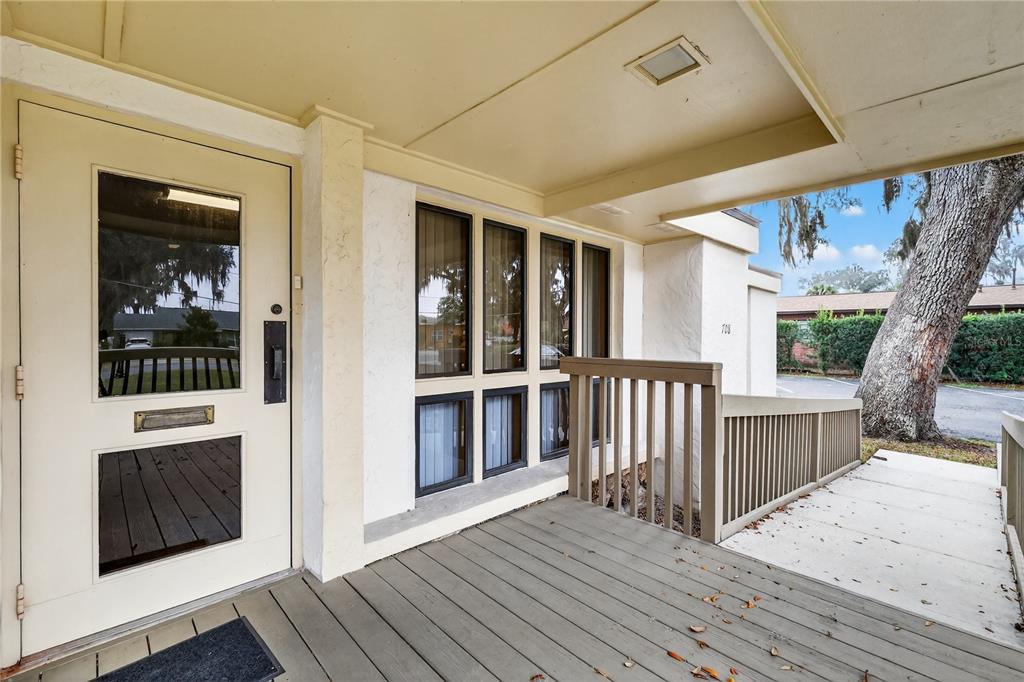 A covered wooden porch leads to a white door with a window and a mail slot — 708 LEE STREET, LEESBURG, FL
