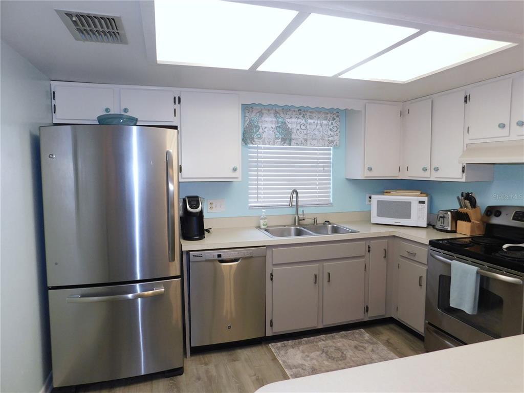 A kitchen features stainless steel appliances, white upper cabinets, grey lower cabinets, and a window — 1400 TARPON WOODS BOULEVARD UNIT 1-4, PALM HARBOR, FL