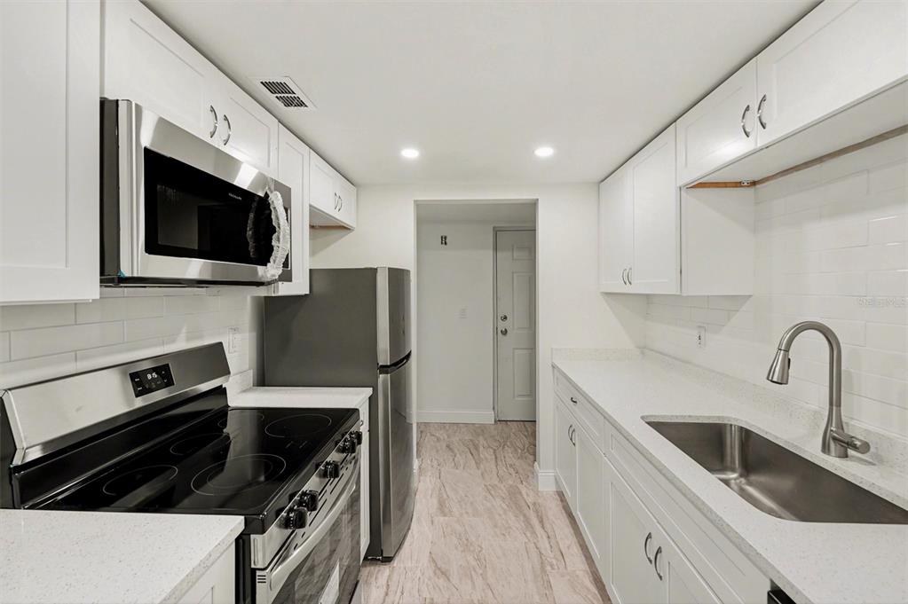 A galley kitchen features white cabinets, stainless steel appliances, a subway tile backsplash, and countertops — 11409 8TH STREET N UNIT 1507, ST PETERSBURG, FL