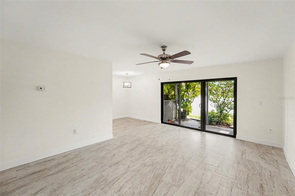 A living room with light wood-look tile flooring, a ceiling fan, and sliding glass doors — 11409 8TH STREET N UNIT 1507, ST PETERSBURG, FL