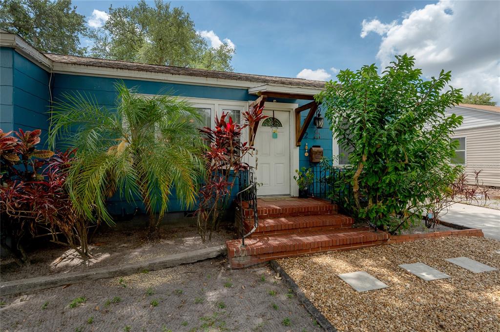 A blue house exterior features a brick front porch, tropical landscaping, and a gravel yard — 912 CORNELIUS AVENUE, TAMPA, FL