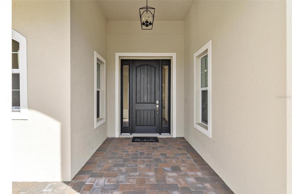 A covered entryway features a dark front door with sidelights, a lantern light, and pavers — 39634 GROVE HEIGHTS, LADY LAKE, FL