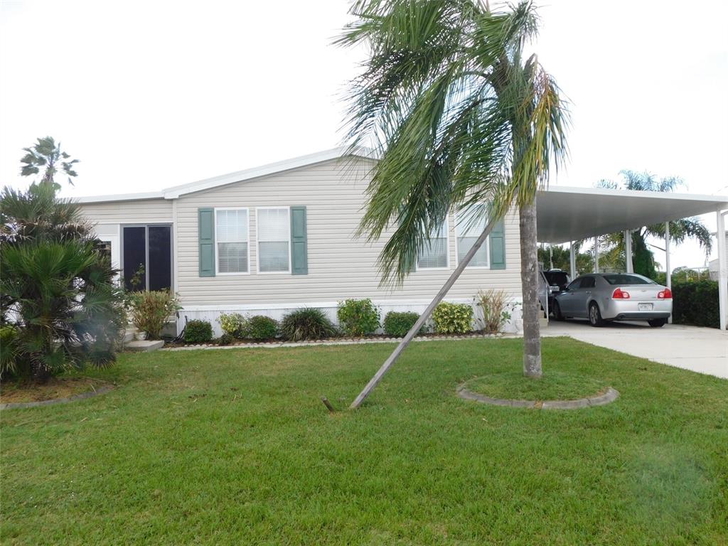 A single-story manufactured home with light siding, green shutters, and a carport over a driveway — 11739 SW LEMON AVENUE, ARCADIA, FL