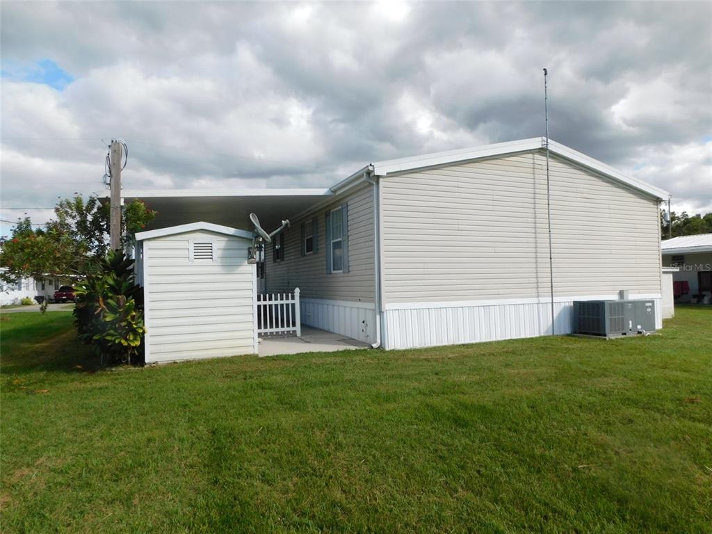 The exterior of a light-colored mobile home features a carport, a storage shed, and siding — 11739 SW LEMON AVENUE, ARCADIA, FL