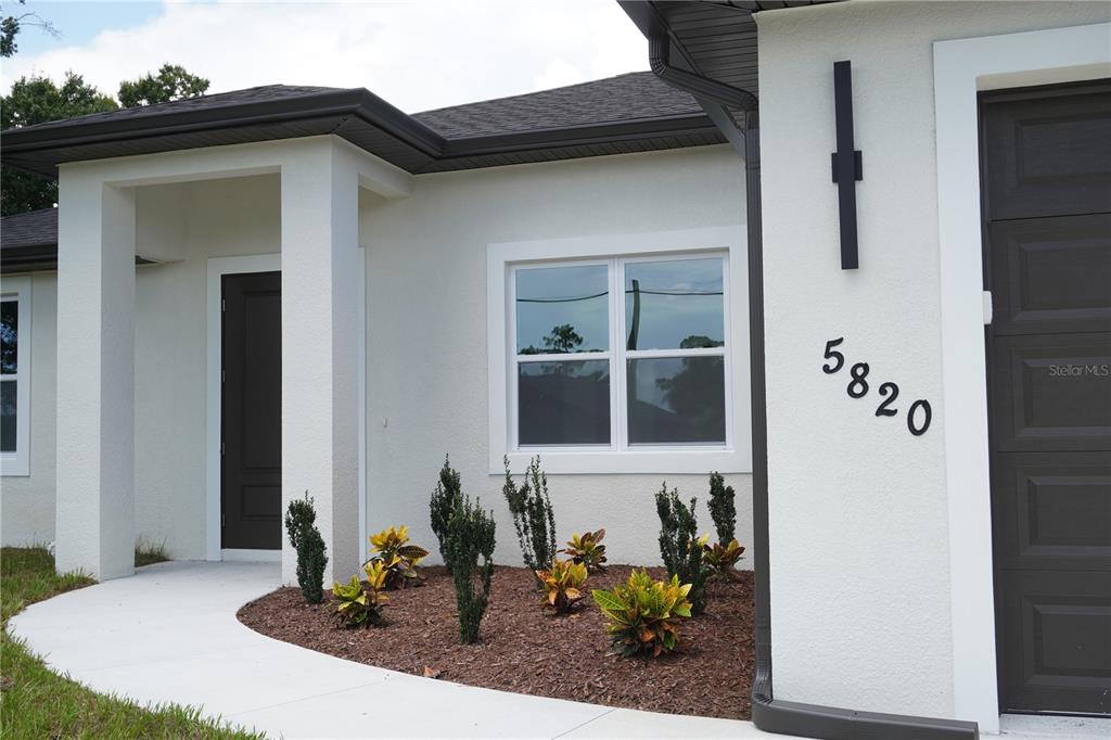 The exterior of a house features a white stucco facade, a dark door, and landscaping — 5820 BRICKELL DRIVE, NORTH PORT, FL