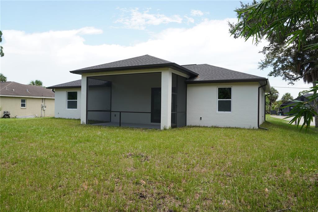 A rear view of a single-story house featuring a screened-in patio and a grassy yard — 5820 BRICKELL DRIVE, NORTH PORT, FL