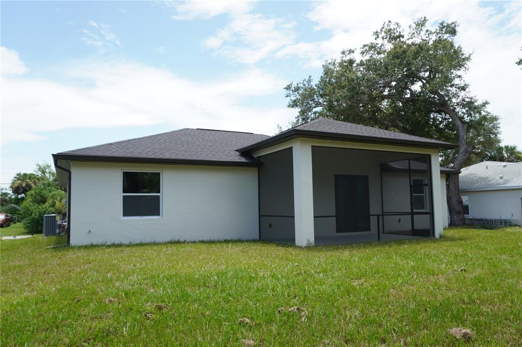 The rear exterior of a single-story house features a screened-in patio and a grassy yard — 5820 BRICKELL DRIVE, NORTH PORT, FL