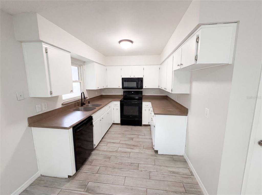 A kitchen features white cabinets, brown countertops, black appliances, and light wood-look tile flooring — 2922 XAVIER COURT, ORLANDO, FL
