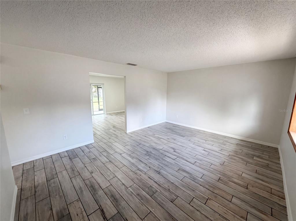 An empty room with light-colored walls and wood-look tile flooring leads to an adjacent space — 2922 XAVIER COURT, ORLANDO, FL