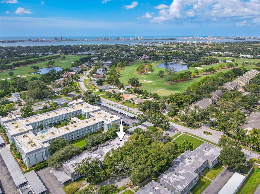 An aerial view shows a multi-story apartment complex surrounded by trees and a golf course — 1708 BELLEAIR FOREST DRIVE UNIT D, BELLEAIR, FL