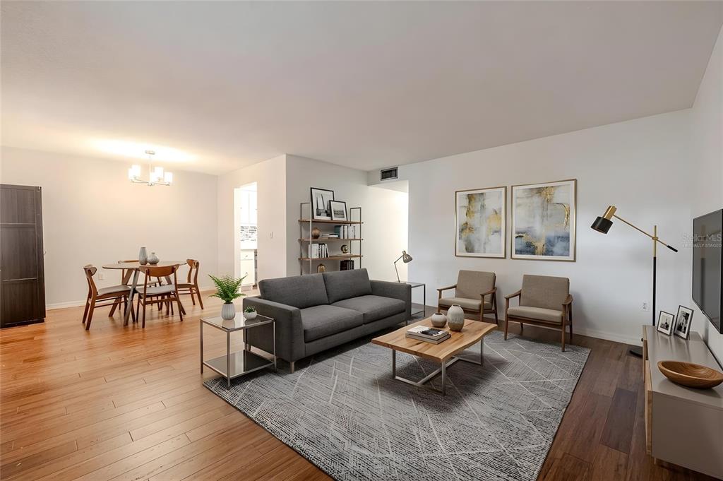 A living room and dining area with hardwood floors, a gray sofa, and area rug — 1708 BELLEAIR FOREST DRIVE UNIT D, BELLEAIR, FL
