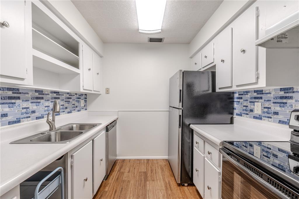 A galley kitchen features white cabinets, stainless steel appliances, and a blue mosaic tile backsplash — 1708 BELLEAIR FOREST DRIVE UNIT D, BELLEAIR, FL