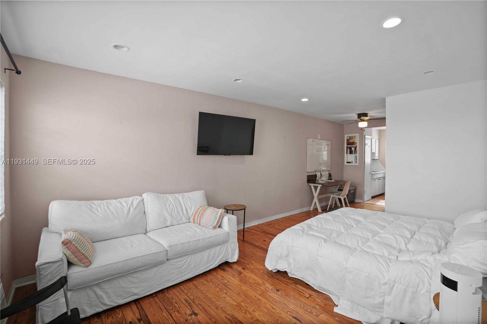 A studio apartment features a white sofa, a bed, and a small desk on wood floors — 200 76th St # 56, Miami Beach FL 33141, MIAMI BEACH, FL