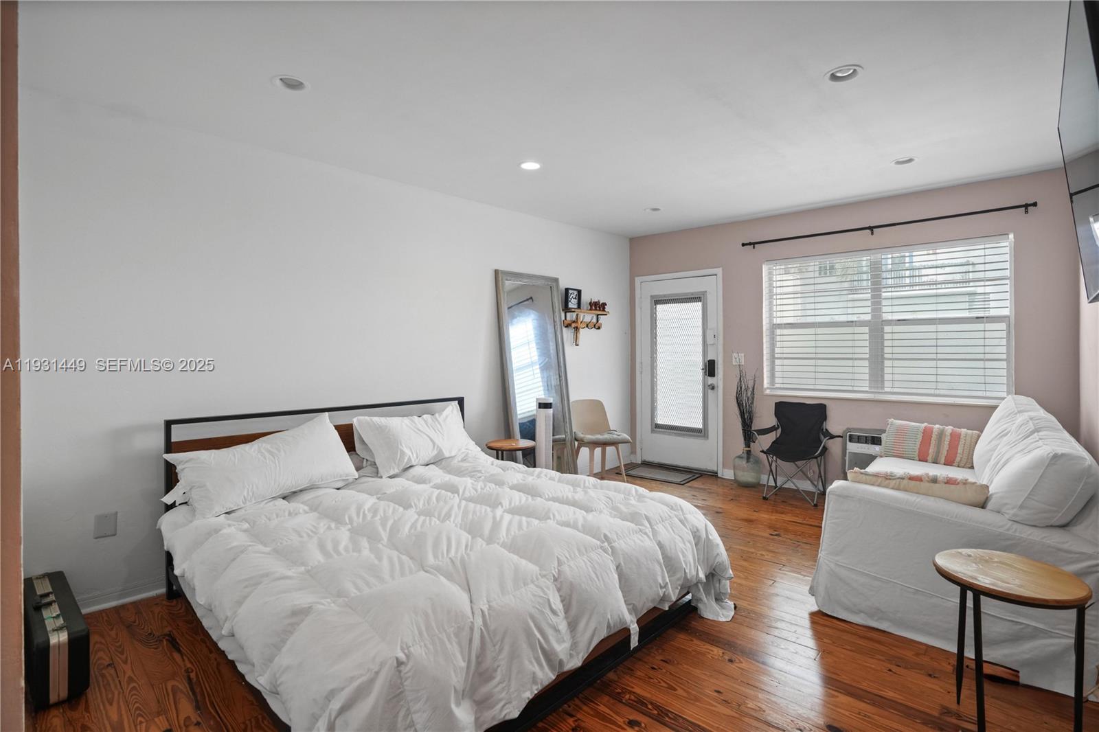 A bedroom features a bed with white bedding, hardwood floors, a mirror, and a sofa — 200 76th St # 56, Miami Beach FL 33141, MIAMI BEACH, FL