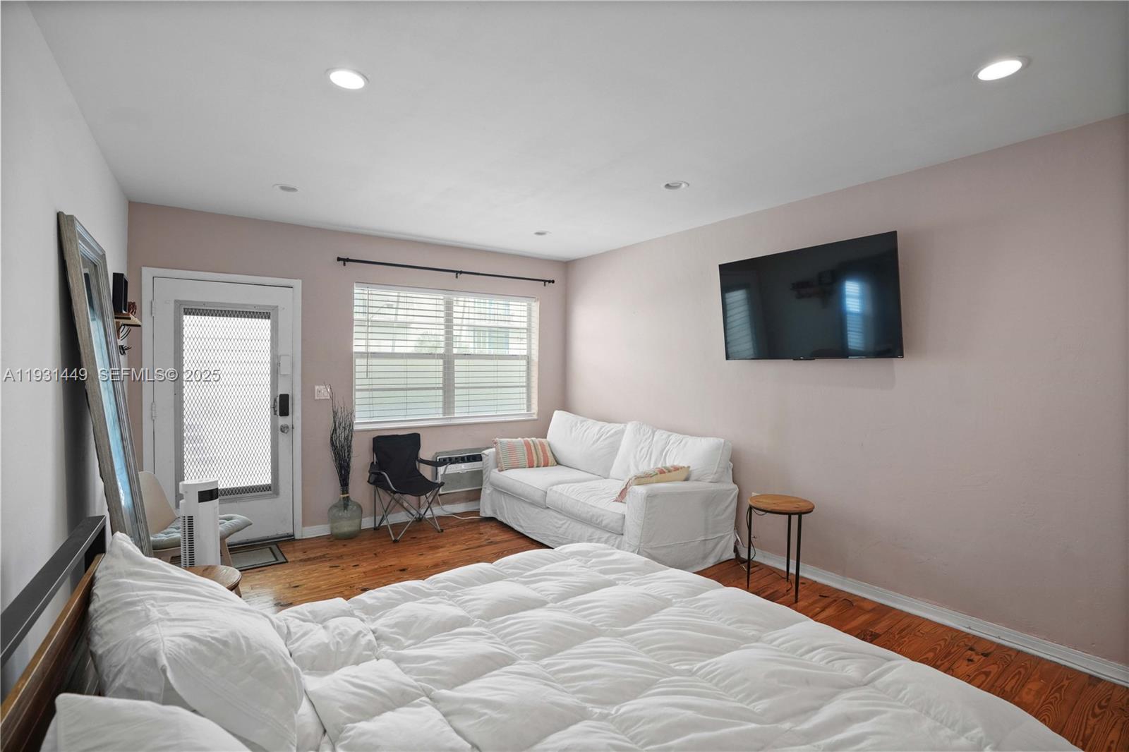 A bedroom features a white sofa, a bed, a wall-mounted television, and wood flooring — 200 76th St # 56, Miami Beach FL 33141, MIAMI BEACH, FL