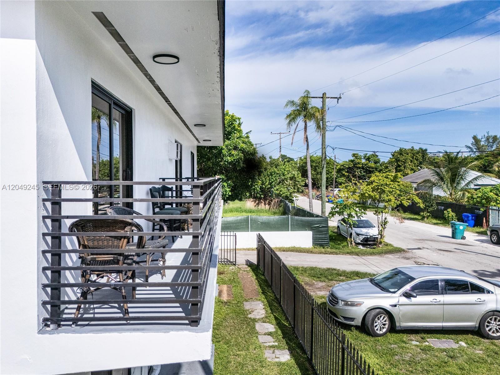 A white building features a balcony with black railings overlooking a street and parked cars — 131 NE 77th St, Miami FL 33138, MIAMI, FL