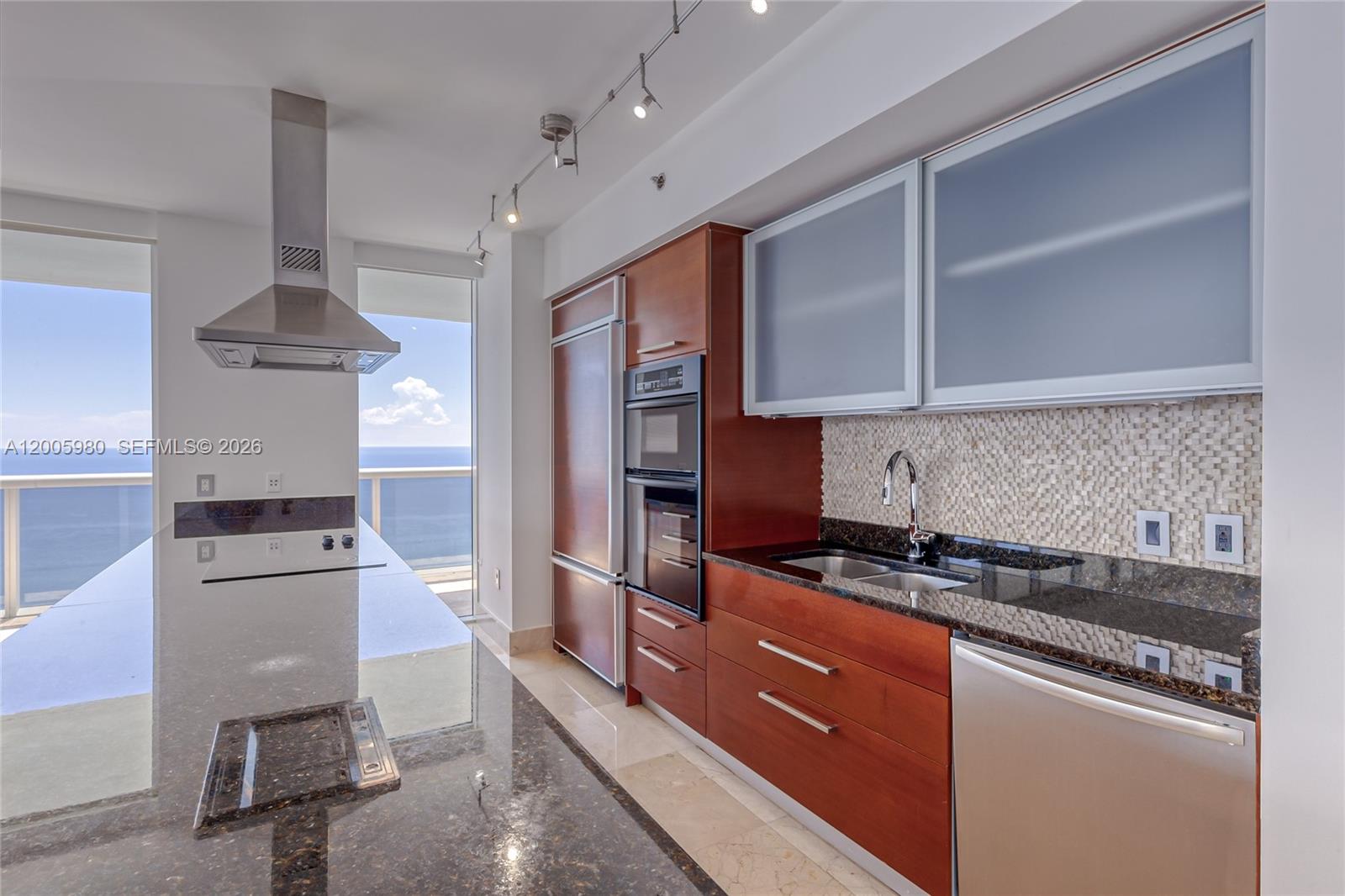 A modern kitchen features wood cabinetry, dark granite countertops, stainless steel appliances, and ocean views — 1830 S Ocean Dr # 4601, Hallandale Beach FL 33009, HALLANDALE BEACH, FL