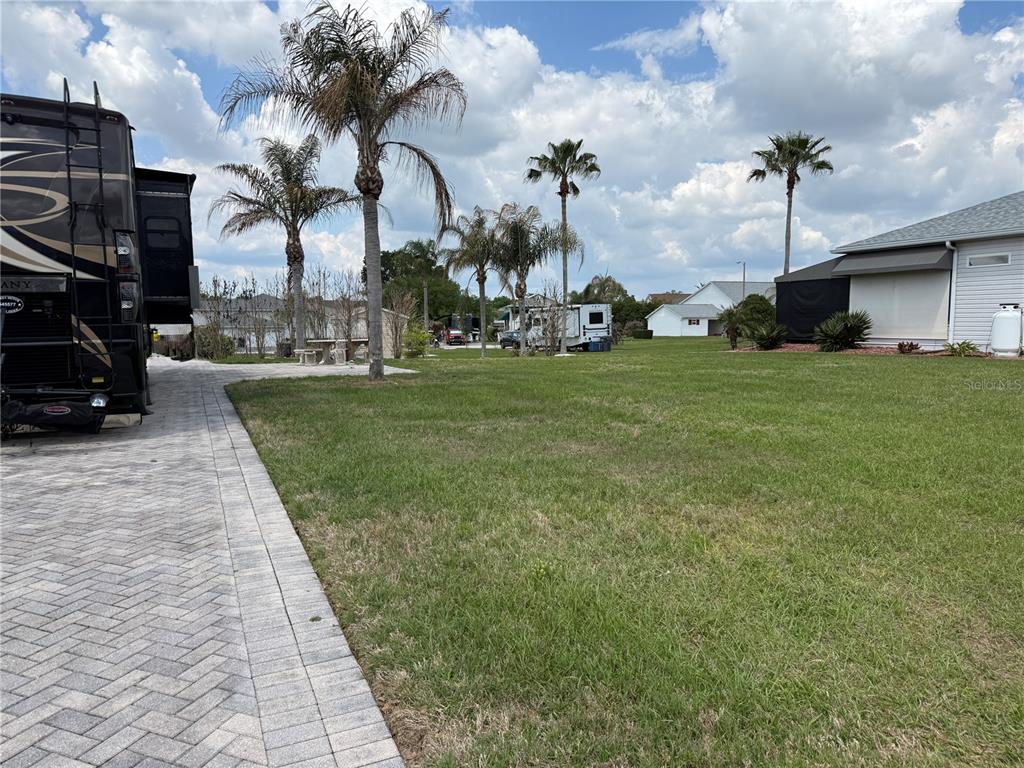 A large grassy yard features a paved driveway, palm trees, and parked recreational vehicles — 1030 RALLY DRIVE, POLK CITY, FL