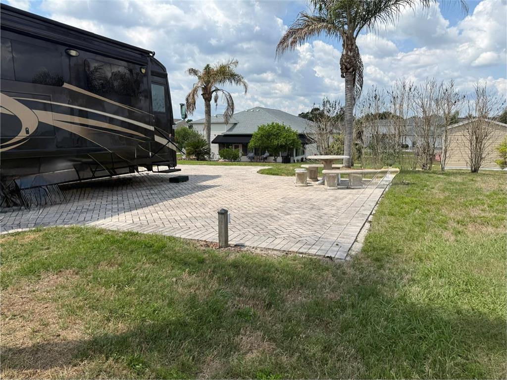 A large RV is parked on a paved brick patio next to a stone table — 1030 RALLY DRIVE, POLK CITY, FL