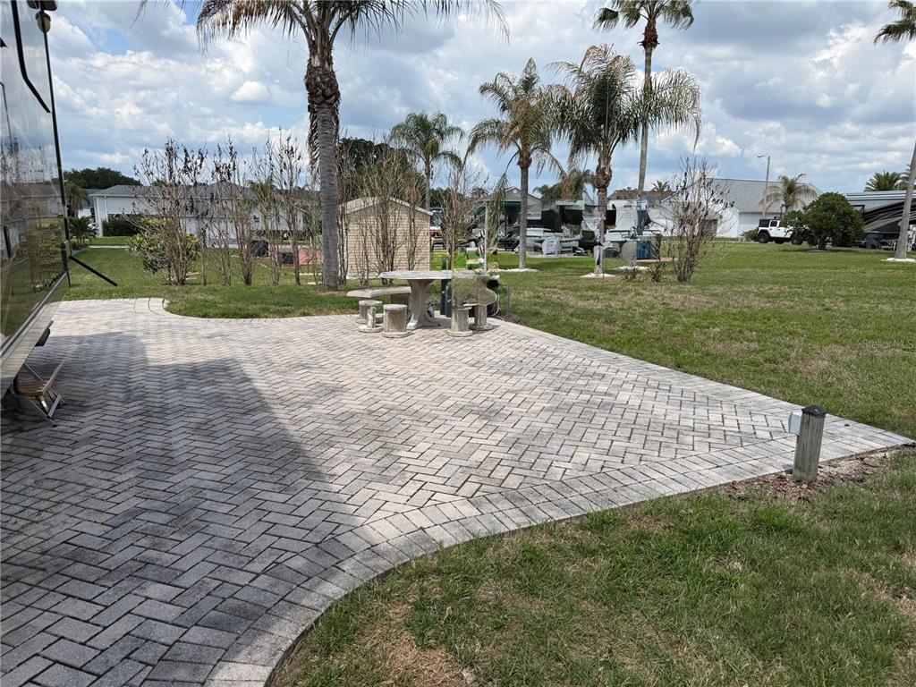 A paved patio with a stone table and benches sits beside an RV in a yard — 1030 RALLY DRIVE, POLK CITY, FL