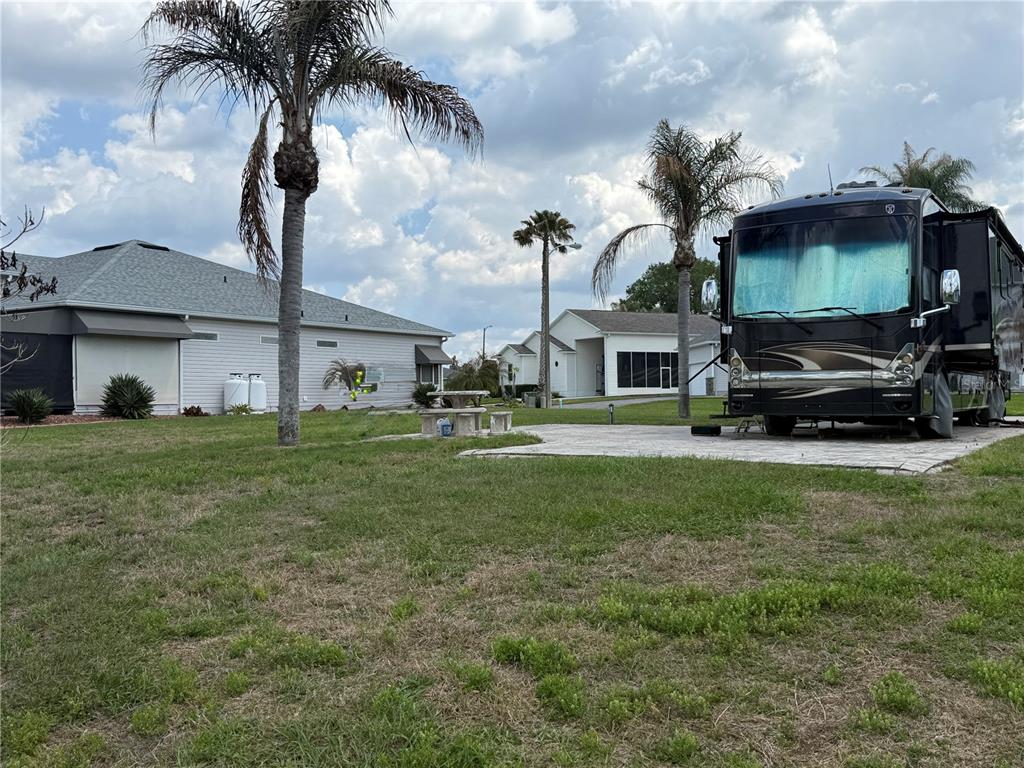 A large recreational vehicle is parked on a paved pad next to a residential house — 1030 RALLY DRIVE, POLK CITY, FL