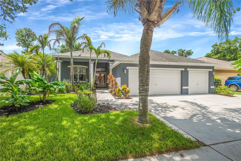 A single-story house with a gray exterior, three-car garage, and palm trees in the yard — 1128 LUMSDEN TRACE CIRCLE, VALRICO, FL