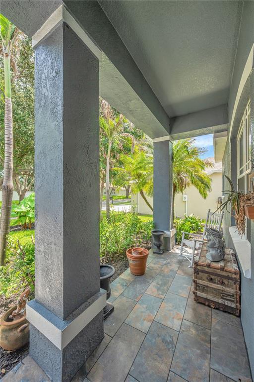 A covered porch features gray stucco columns, tile flooring, and potted plants — 1128 LUMSDEN TRACE CIRCLE, VALRICO, FL