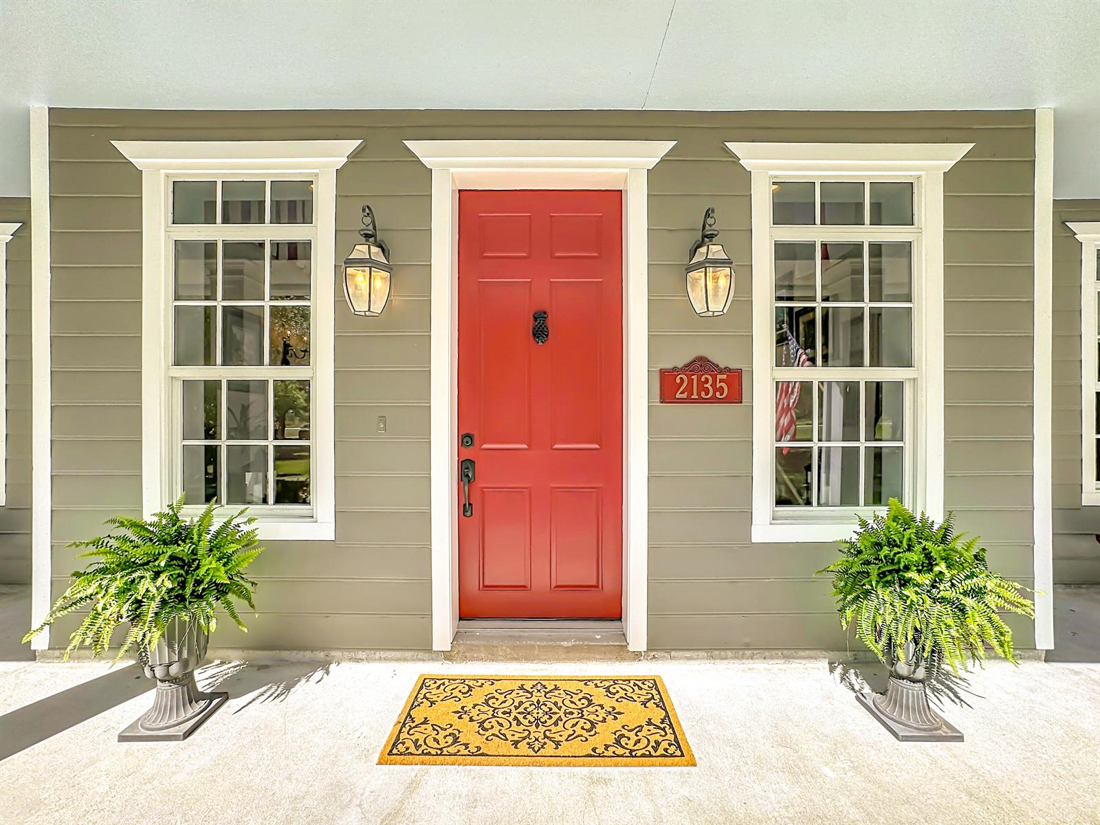 A red front door is flanked by two windows, wall lanterns, and potted ferns — 2135 55th Avenue SW, Vero Beach FL 32968, VERO BEACH, FL