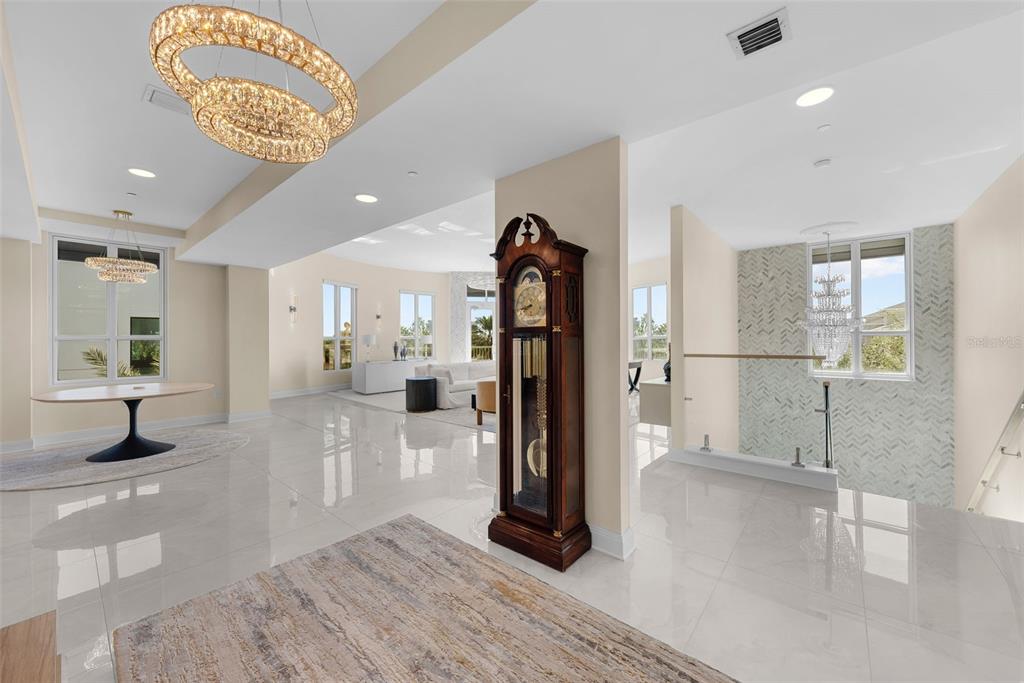 A spacious, open-concept living area features polished tile floors, a grandfather clock, and modern chandeliers — 450 KNIGHTS RUN AVENUE UNIT 405, TAMPA, FL