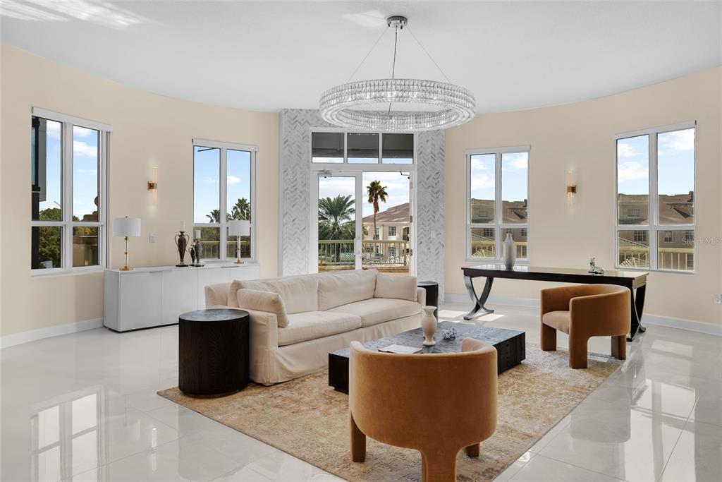 A bright living room features a white sofa, two tan chairs, and a crystal chandelier — 450 KNIGHTS RUN AVENUE UNIT 405, TAMPA, FL